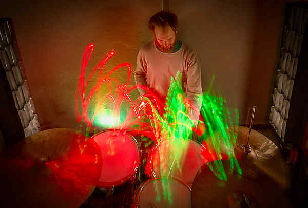 Langzeitbelichtung eines Schlagzeugspielers, im Proberaum, an seinem Schlagzeug mit Grün und rotem Licht.
