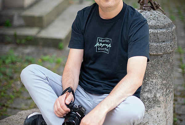  Portrait eines Fotografen auf einer Treppe in Würzburg im Stadtgebiet bleich, schwarzen T-Shirt und Zopf und Haare hochgebunden, Martin Rothe Fotografie
