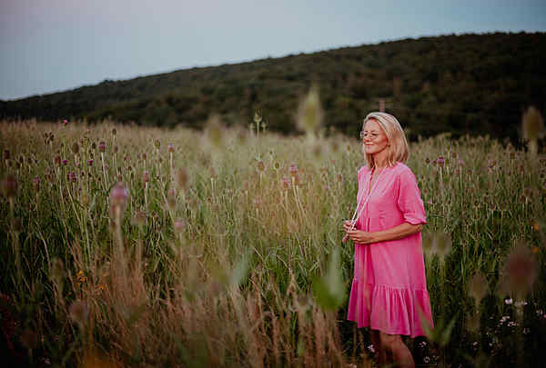Blonde Frau im Distelfeld bei Sonnenuntergang mit magenta farbenen Kleid fast an eine Malakette