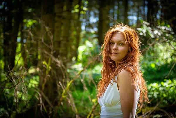 Sie mit roten Haaren steht im mystischen Wald und schaut in die Kamera