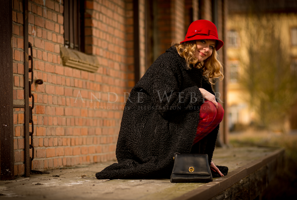 Nostalgisch gekleidete Frau,  mit schwarzen Mantel, steht an einem Bahnsteig in Seligenstadt bei Würzburg mit rotem Hut 