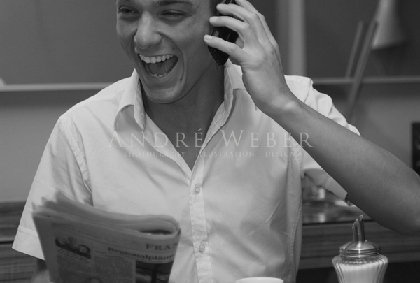 Mann mit Zeitung lachend am Kaffeetisch