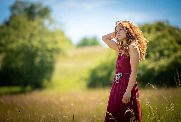 Frau mit roten Haaren langt sich durchs Haar Sonnenschein auf einem Feld