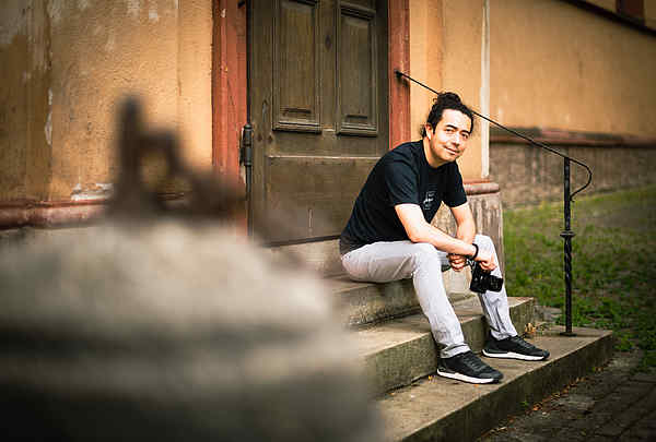 Portrait eines Fotografen auf einer Treppe in Würzburg im Stadtgebiet bleich, schwarzen T-Shirt und Zopf und Haare hochgebunden, Martin Rothe Fotografie